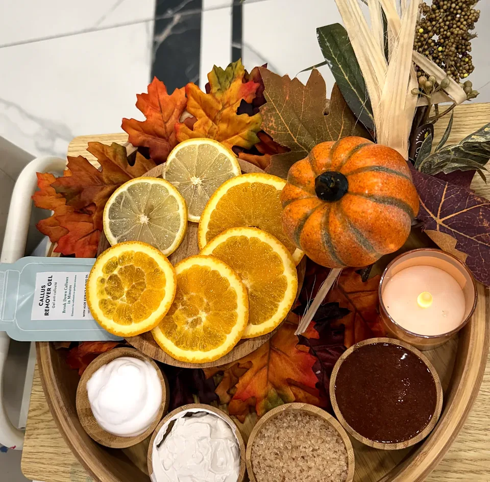 Pedicure tray with fresh citrus slices, callus remover gel, candle and wooden care bowls
