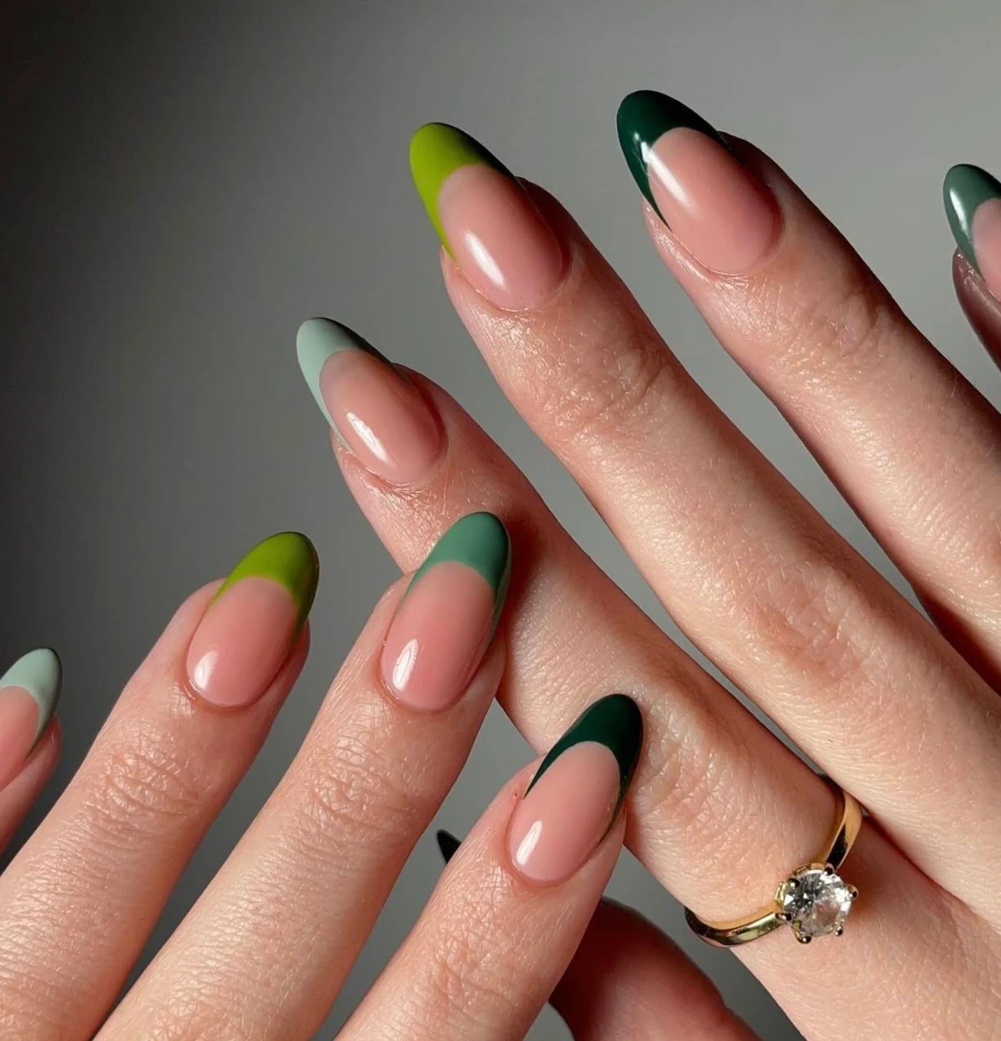 Finished almond nails with nude bases, varied green French tips and a gold ring